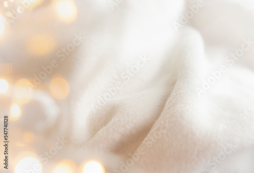 Atmospheric background with detail of a fluffy, comfortable fabric blanket and twinkling lights. Cosy winter, Christmas concept.