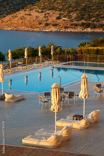 Foto Luxury morning swimming pool with empty deck chairs, tables and umbrellas at the resort with beautiful sea view