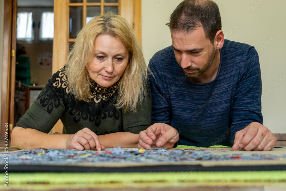 Fototapeta premium Adorable couple doing a puzzle lying on the floor, they enjoy their company while spending some fun time together.