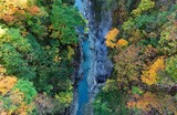 Aerial view of beautiful Oyasukyo Hot Spring Gorge (小安峡温泉) in Akita, Japan, with colorful autumn foliage on vertical rocky cliffs and tourists hiking by the stream at bottom of the deep valley