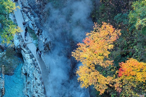 Aerial view of Oyasukyo Hot Spring Gorge with colorful autumn foliage on vertical rocky cliffs & tourists hiking by the stream at bottom of the gorge in Akita Japan ~ Beautiful fall scenery of Japan