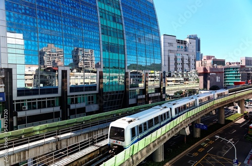 View of a train traveling on elevated rails of Taipei Metro System by a modern building of glass curtain walls on a beautiful sunny day   View of MRT railways in Taipei  the capital city of Taiwan