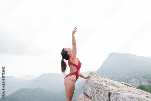 mature caucasian brunette woman with long hair a red top exercising leaning on a large mountain rock