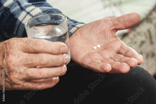 Fototapeta An elderly man holds pills and a glass of water in his hands
