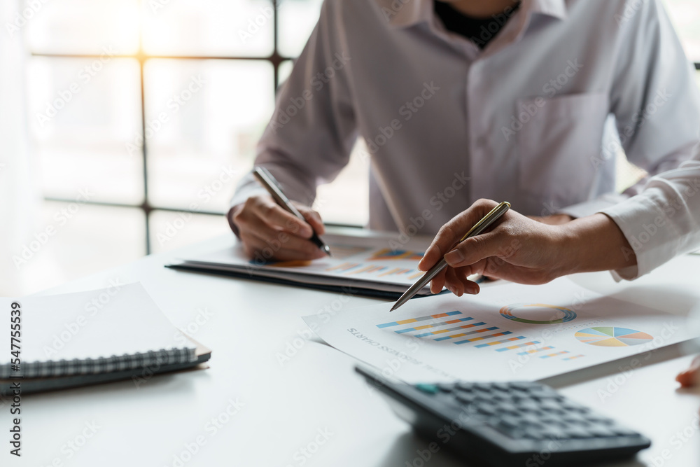 Two business people point to graphs and charts to analyze market data, balance sheet, account, net profit to plan new sales strategies to increase production capacity. - obrazy, fototapety, plakaty 