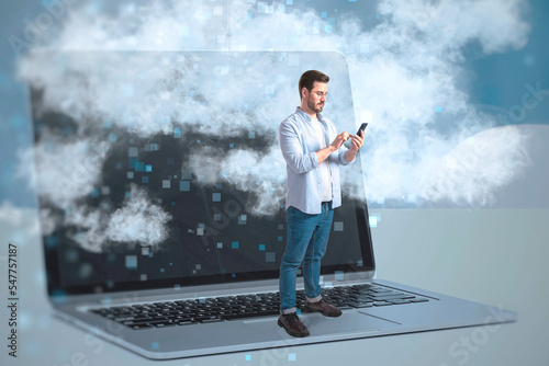 Abstract image of businessman standing on laptop keyboard and using cellphone on desktop workplace with clouds. Remote work, VR, technology and innovation concept. photo