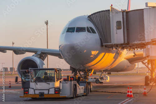 Aircraft is attached to the terminal gangway of the airport building preparation for towing and launch flight in the evening at sunset.