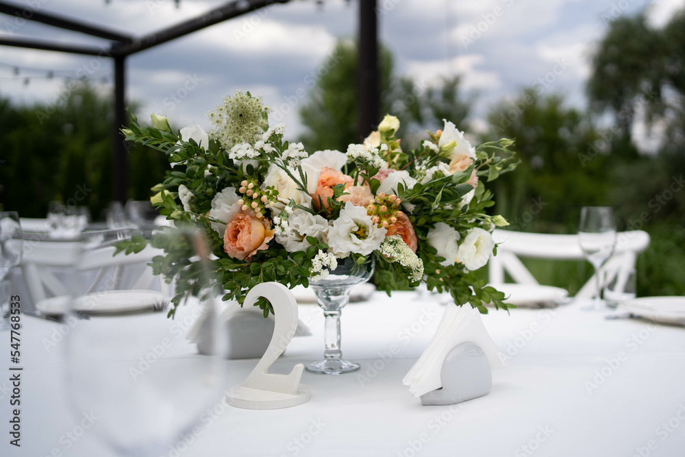Table centerpiece with white and peach rustic floral arrangement in glass vase. Rustic wedding table.
