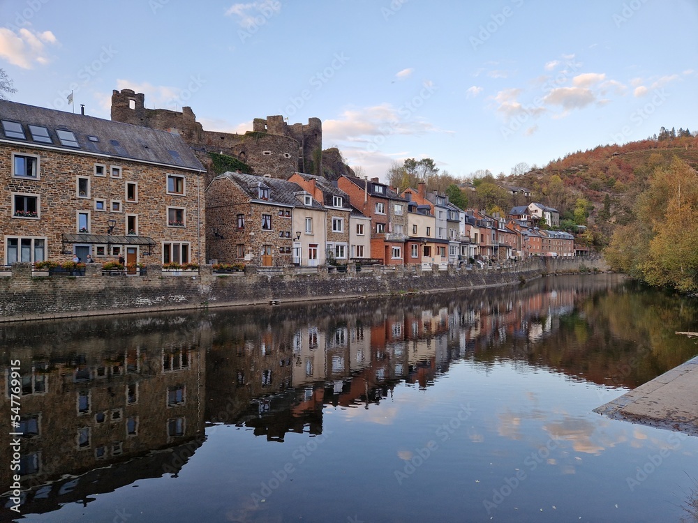 Riverbank of picturesque village of La Roche En Ardenne (Belgian Ardennes) along the river Ourthe at golden hour (sunset) with reflection of stone houses in the water