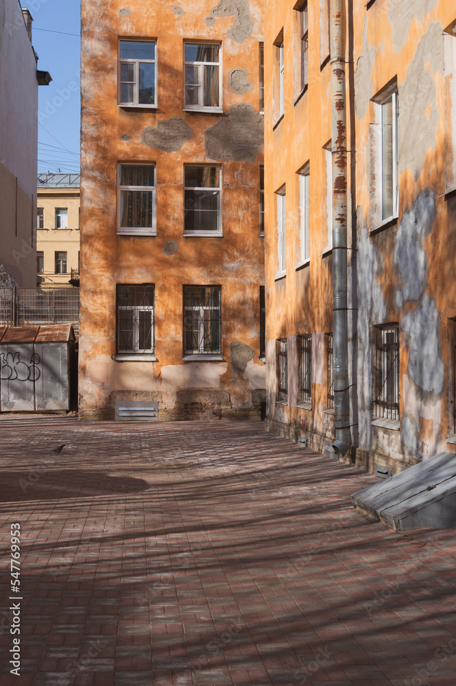 courtyard of an old stone orange house. shadows of trees on the ground and walls. St. Petersburg, Petrogradskaya