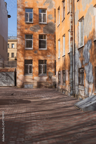 courtyard of an old stone orange house. shadows of trees on the ground and walls. St. Petersburg, Petrogradskaya