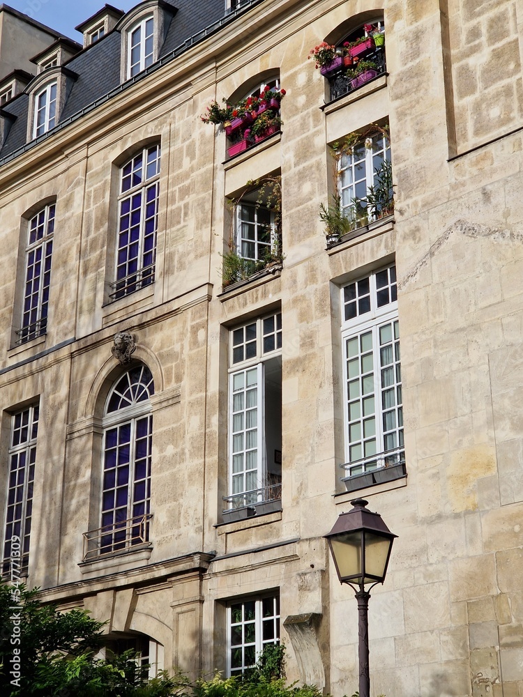 Typical Paris facade of old stone building with high windows, flowers and a lantern on sunny day in France