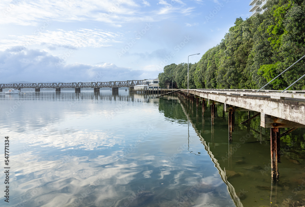 White leading lines of long pier along coastline to historic railway bridge