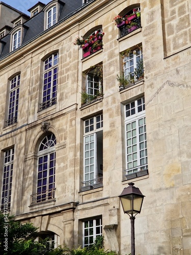 Typical Paris facade of old stone building with high windows, flowers and a lantern on sunny day in France