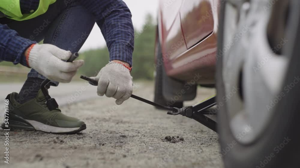 Jack under the car. male hands turn the knob to replace a punctured wheel. Installing a spare wheel. A man in a road vest. Weighing the car for repairs on the road. High quality 4k footage Jack under the car. male hands turn the knob to replace a punctured wheel. Installing a spare wheel. A man in a road vest. Weighing the car for repairs on the road. High quality 4k footage