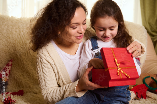 Wallpaper Mural Multi-ethnic pretty woman in warm beige sweater, a loving mother hugging her adorable lovely daughter, while giving her a cute Christmas present. Happy childhood. Winter and New Year's holidays Torontodigital.ca
