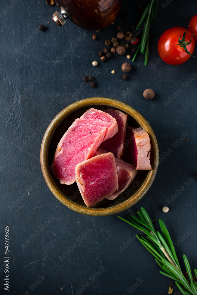 Pieces of tuna in a bowl with rosemary and spices on a dark background.