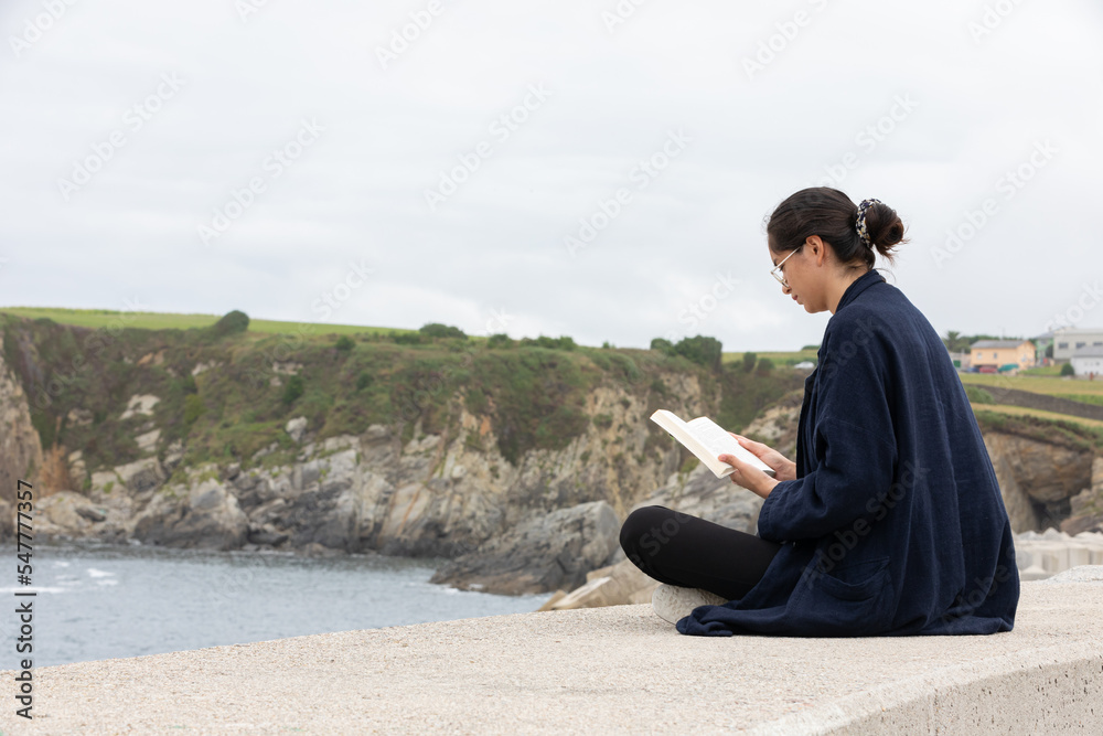 Side view of female in casual clothes reading book near sea Side view of female in casual clothes reading book near sea