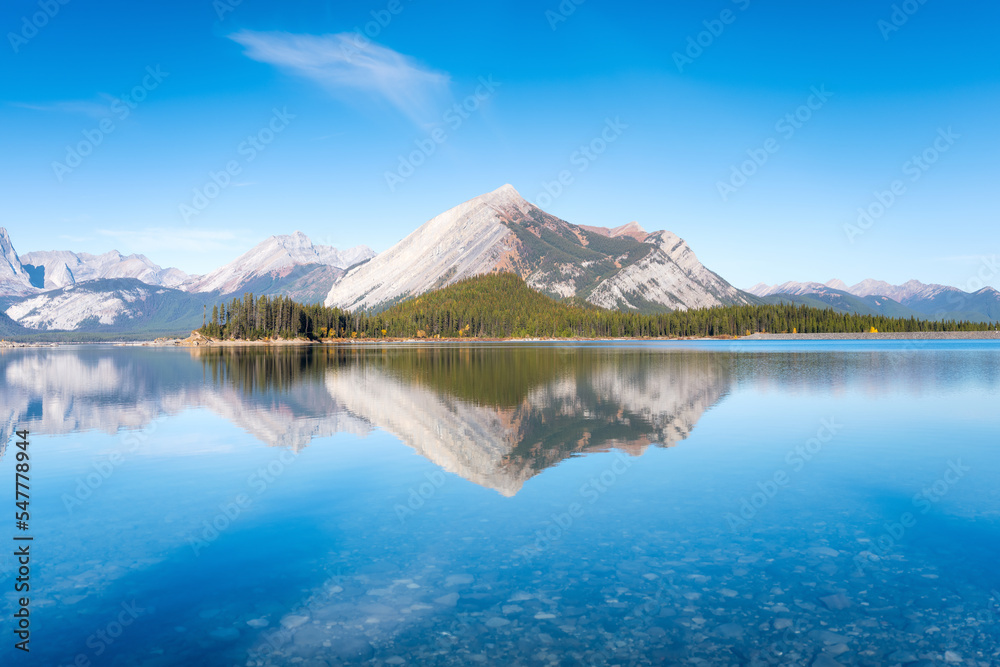 Mountain landscape at the day time. Lake and forest in a mountain valley. Natural landscape with a blue sky. Reflections on the surface of the lake. Banff National Park, Alberta, Canada.