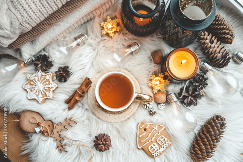 Christmas holiday decor flat lay top view, cup of tea, burning candles, gingerbread, cones and cinnamon on a fluffy plaid