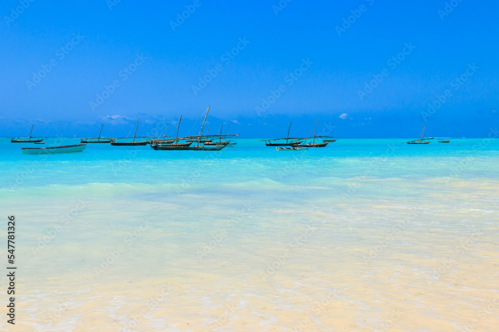 View of tropical sandy Nungwi beach and traditional wooden dhow boats in the Indian ocean on Zanzibar, Tanzania View of tropical sandy Nungwi beach and traditional wooden dhow boats in the Indian ocean on Zanzibar, Tanzania
