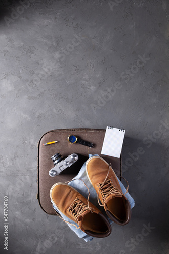 Old boots and trip stuff kit on suitcase at floor background. Travel concept idea