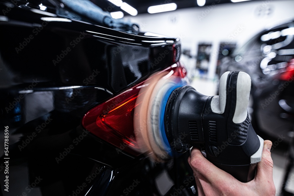 Employee of a car detailing studio polishes the paint of a car with an electric polishing machine
