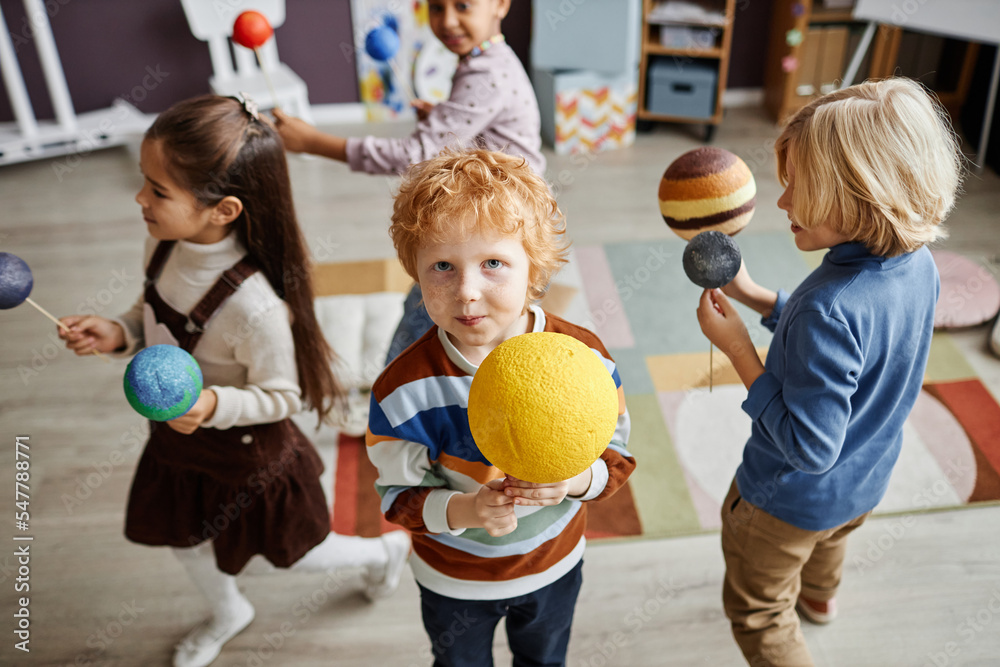Fototapeta premium Selective focus on cute little boy holding model of sun while playing with group of kids and learning solar system in nursery school