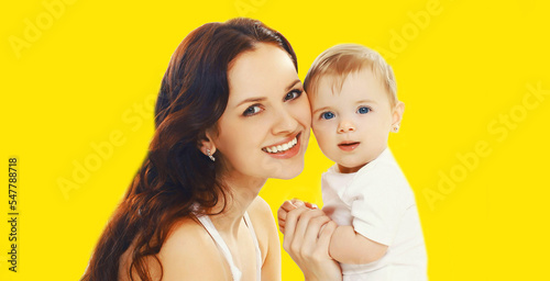 Portrait of happy smiling mother holding her baby isolated on yellow background