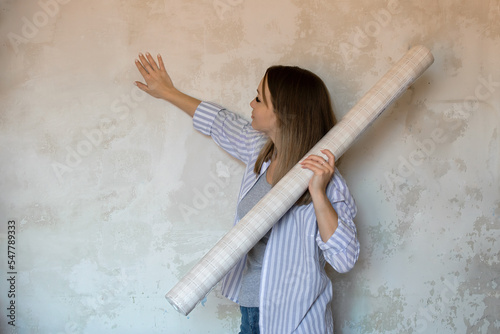 Repair and improvement of the house. a beautiful girl holds wallpaper in her hands, which she is going to stick on the wall with her own hands