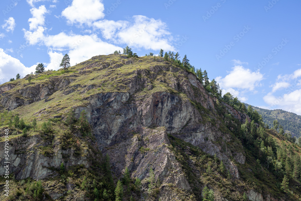 A large mountain with a sheer cliff close-up against the sky. Hiking tourism. Mountains of the Altai Mountains, Altai Republic