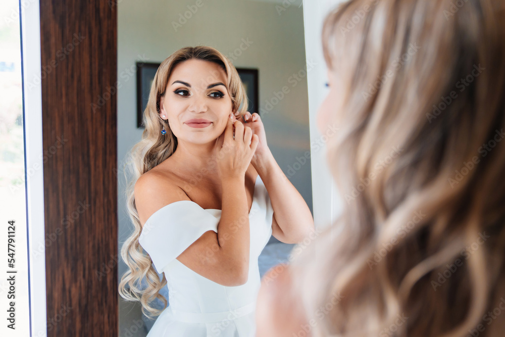 close up. bride in a white dress looks at the reflection and puts on earrings. close up. bride in a white dress looks at the reflection and puts on earrings.