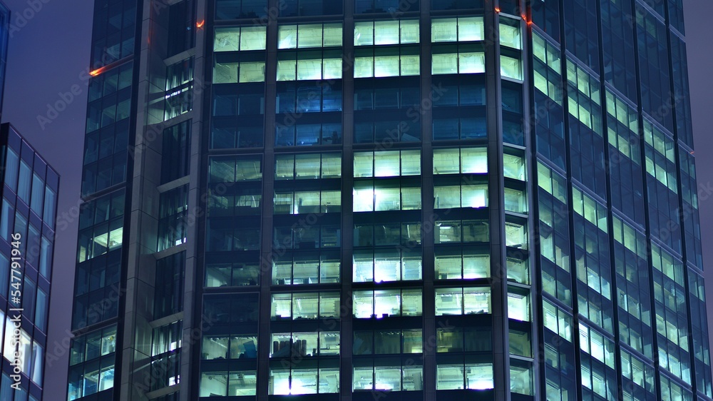 Modern office building in city at the night. View on illuminated offices of a corporate building. Blinking light in window of the multi-storey building of glass and steel. Long exposure at night Modern office building in city at the night. View on illuminated offices of a corporate building. Blinking light in window of the multi-storey building of glass and steel. Long exposure at night