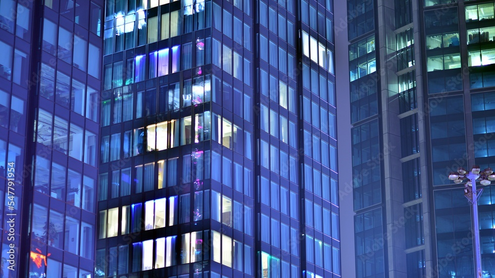 Modern office building in city at the night. View on illuminated offices of a corporate building. Blinking light in window of the multi-storey building of glass and steel. Long exposure at night Modern office building in city at the night. View on illuminated offices of a corporate building. Blinking light in window of the multi-storey building of glass and steel. Long exposure at night
