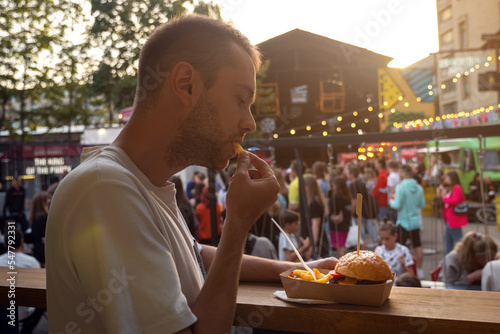 hipster eating burger with french fries on craft paper. man outdoor at food court. street food festival on background blurred photo