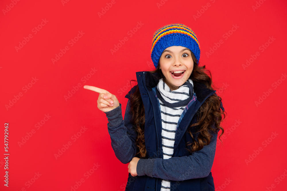 amazed kid with curly hair in hat point finger on copy space. teen girl on red background. amazed kid with curly hair in hat point finger on copy space. teen girl on red background.