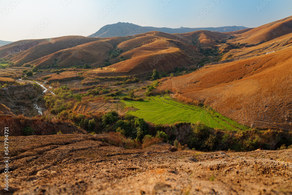 Landscape of Madagascar, typical scenery of the Malagasy countryside with the rice fields, hills and valleys, small simple houses and dry meadows. Devastated environment with great erosion