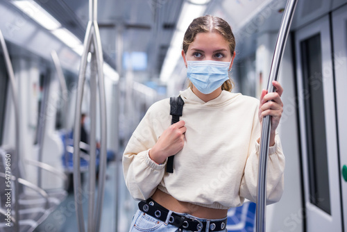 Portrait of a young stylish woman in a face mask riding in a subway wagon