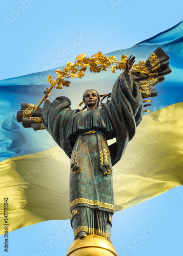 Monument of Independence of Ukraine on background of Ukrainian state flag. Memorial on Maidan Nezalezhnosti, bronze statue of ukrainian woman in national clothes on The Independence Square in Kiev.