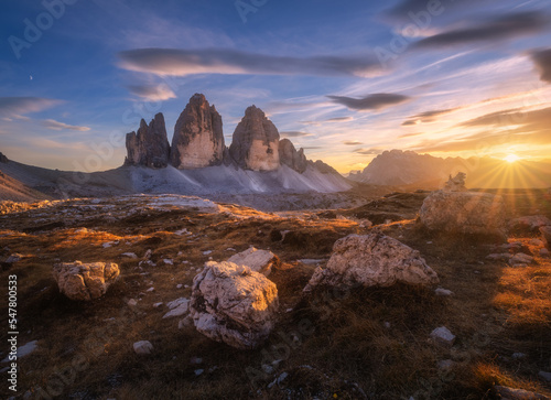 Rocks and stones at colorful sunset in autumn in Tre Cime, Dolomites, Italy. Colorful landscape with mountains, trail, orange grass, blue sky with clouds, golden sunlight in fall. Hiking in mountains 
