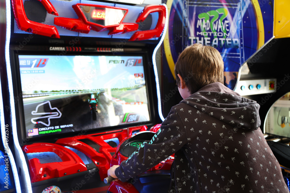 Arcade game room. Video game park for children and teenagers. Boy playing  in video game motorcycle