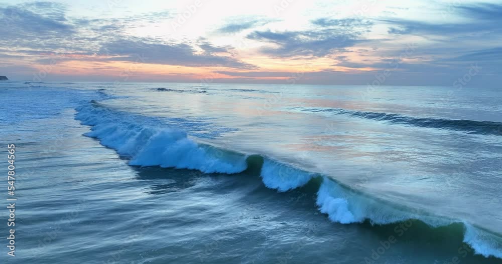 Aerial view of rolling ocean waves at sunset in Portugal. Drone flying over the powerful sea waves with a beautiful sky in background.