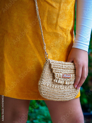 small handbag in the foreground with a woman in a mustard-colored dress 