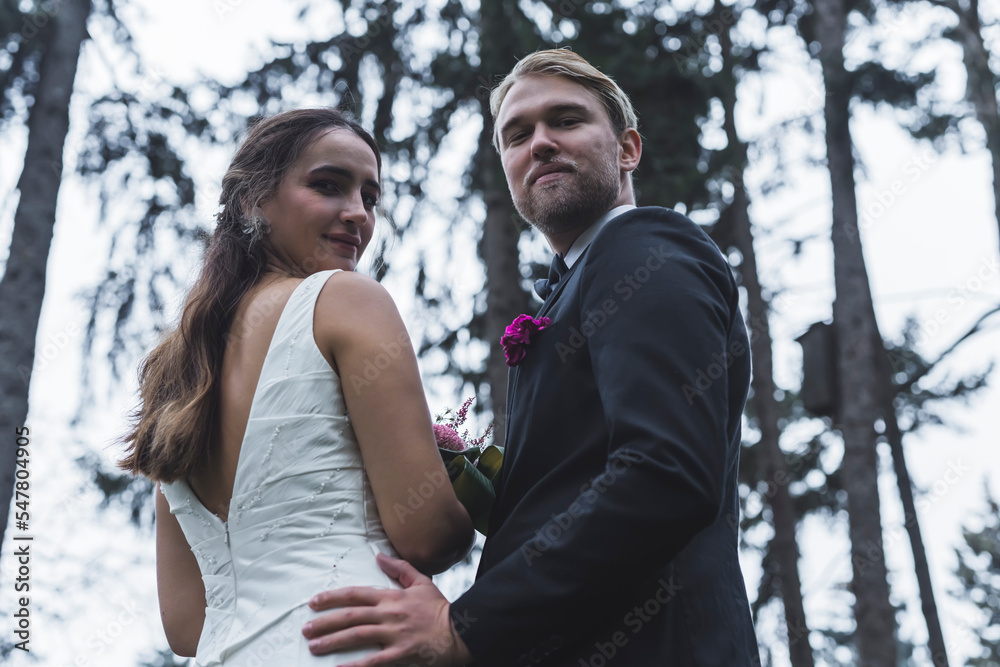 Just married forest photoshoot. Medium portrait of long-haired brunette Turkish bride and her Scandinavian husband looking back at camera with smiles on their faces. . High quality photo Just married forest photoshoot. Medium portrait of long-haired brunette Turkish bride and her Scandinavian husband looking back at camera with smiles on their faces. . High quality photo