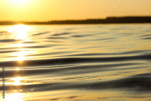 Calm water surface and a horizon view. Soft smooth waves backdrop. The water resource of a river, lake, sea, ocean, body of water. Concept of tranquility, harmony, nature at sunset in yellow sun light © vita