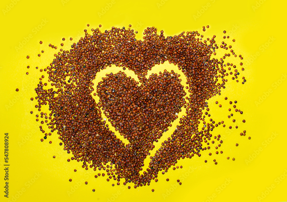 Raw red quinoa seed in heart shape isolated on yellow background.
