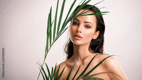 Young beautiful woman with green leaves near face and body. Skin care beauty treatments concept.  Closeup girl's face with green leave. White model with clean, health skin of face - posing at studio