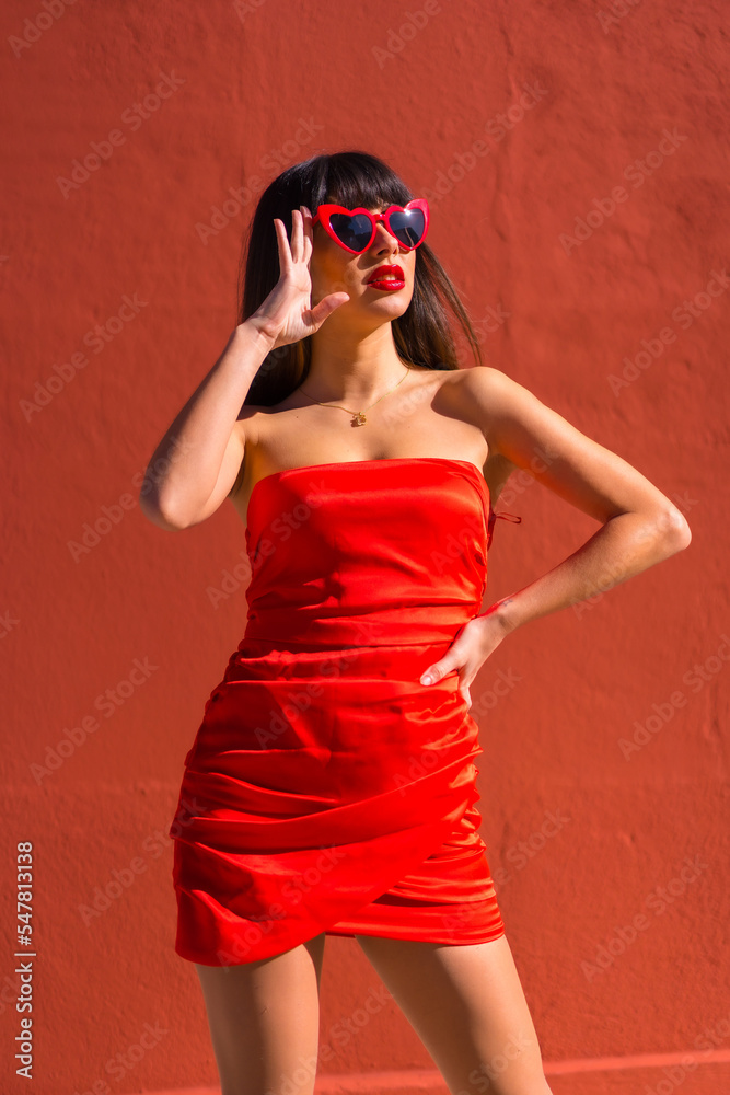 Brunette girl on a red background with hearts glasses and red tight dress, Valentine's Day Brunette girl on a red background with hearts glasses and red tight dress, Valentine's Day