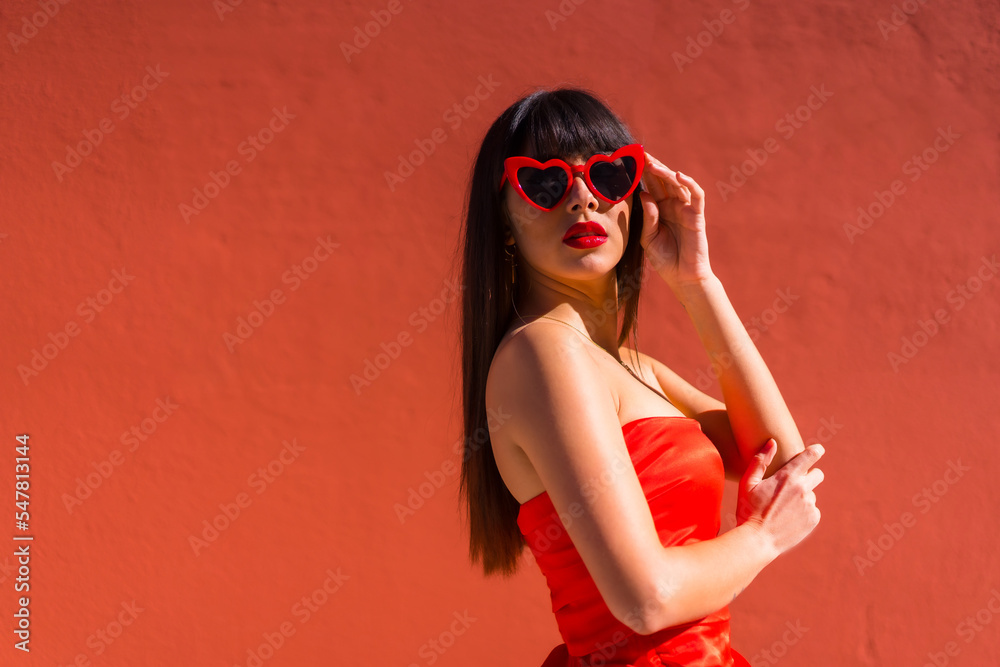 Brunette girl on a red background with hearts glasses and red tight dress, valentine smiling Brunette girl on a red background with hearts glasses and red tight dress, valentine smiling