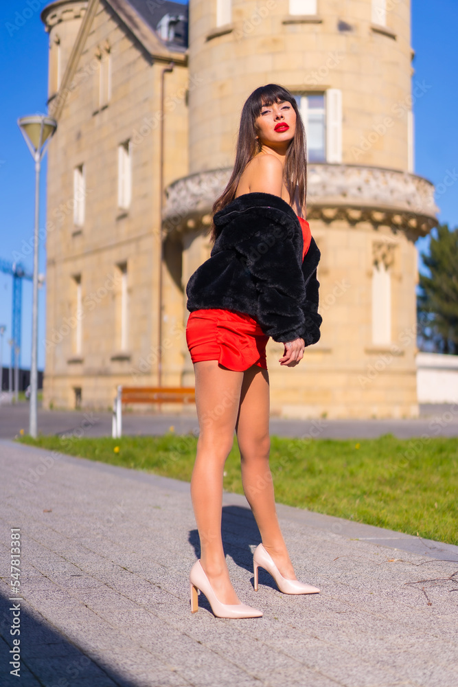 Young woman in a red dress in a beautiful castle, fashionably posing and smiling in a black jacket